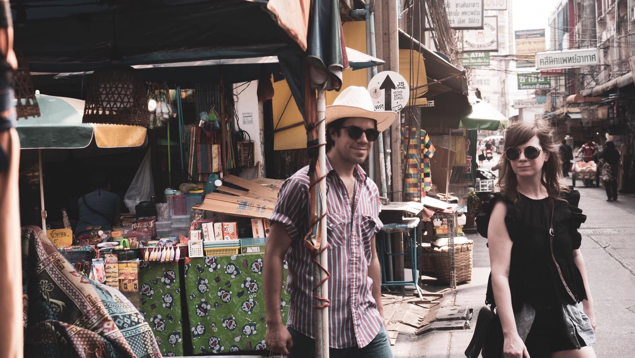 Two musicians walking down a busy market street lined with stalls and signs.