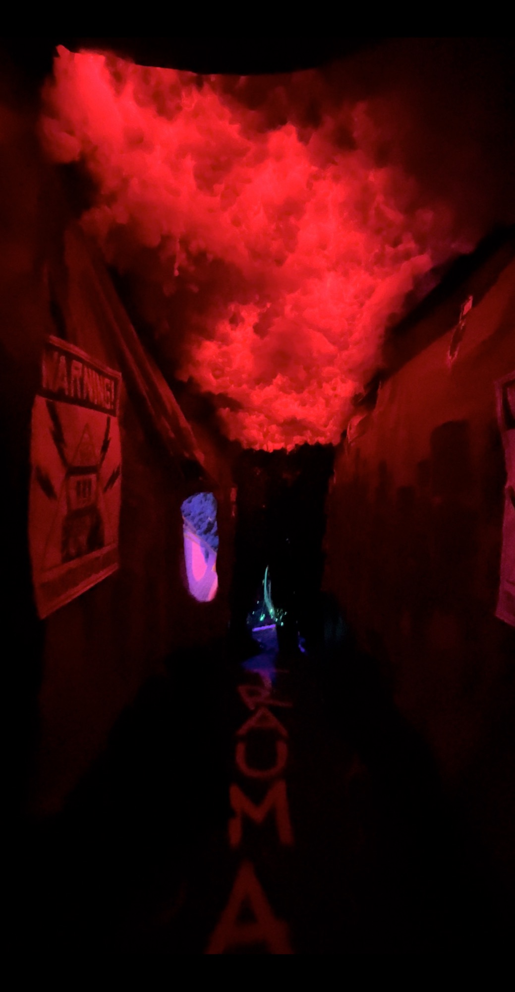 A dark corridor lit red, with a cloud-like canopy overhead, a warning sign on the wall and the word “Trauma” glowing on the floor.