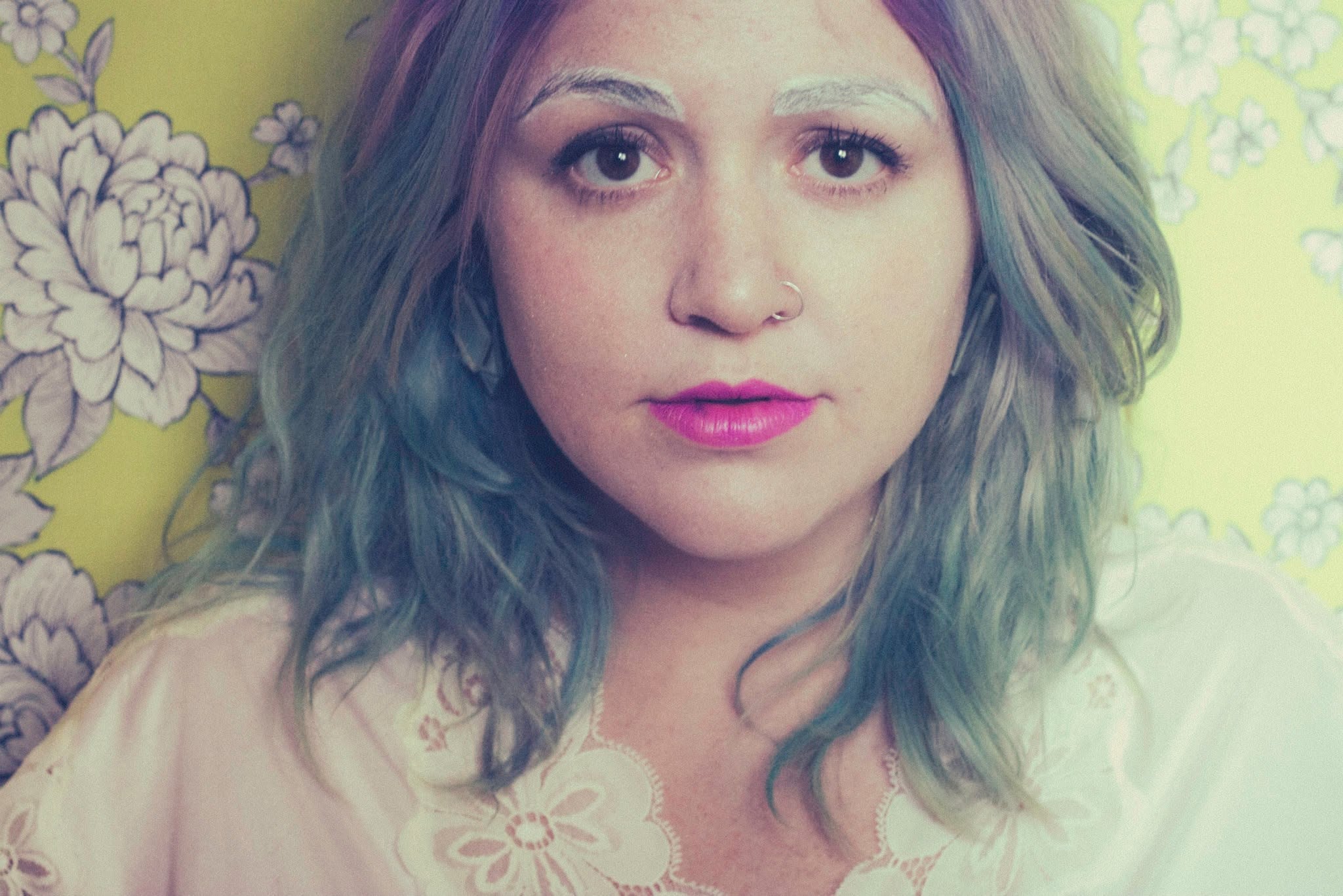 Color close-up of Carrie Fussell in front of floral wallpaper, with bright pink lipstick.