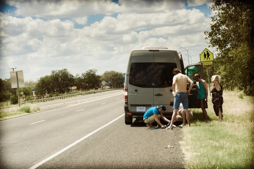 A white van pulled over on the shoulder of a highway as the band stretches their legs.